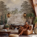A person wearing a matching rust-brown two-piece suit sits in a tan leather lounge chair within a highly styled, bohemian interior featuring a large scenic landscape mural, potted cacti, and warm ambient lighting.