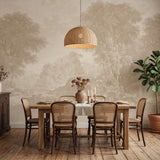 A styled dining room scene with a wooden dining table, six woven-back chairs, a large woven pendant light, a vase of dried flowers, and a large potted plant against a beige wall with a faint scenic landscape mural.