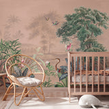 A styled nursery interior featuring a large tropical landscape wallpaper mural with trees, birds, and foliage in muted green, pink, and beige tones. A woven rattan chair with a cream cushion sits beside a light wood crib, with a white plush toy on the floor.