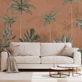 A modern light beige sofa in a styled living room setting, set against a terracotta-colored wall with a tropical palm tree wallpaper pattern. Two round nesting coffee tables are positioned in front of the sofa.